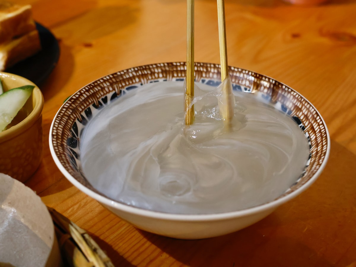 A bowl of noodles in broth being eaten with chopsticks